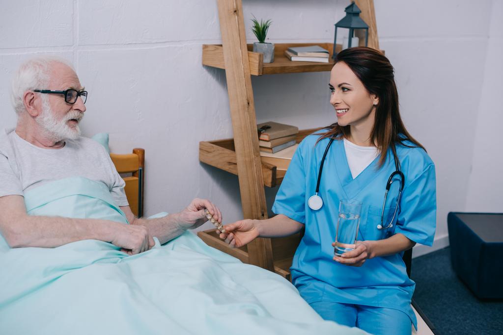 Senior patiënt in bed nemen medicijnen uit vrouwelijke verpleegkundige  - Foto, afbeelding