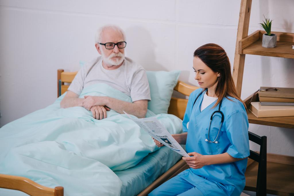 Oude man patiënt kijken van verpleegkundige krant lezen - Foto, afbeelding