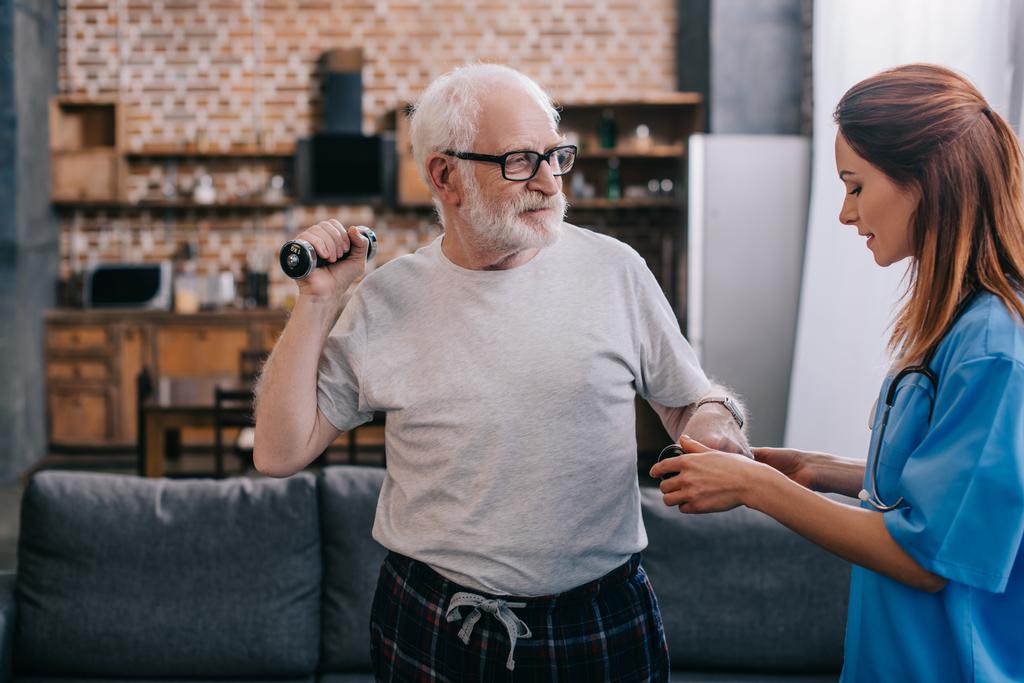 Enfermeira ajudando o homem idoso a se exercitar com halteres
 - Foto, Imagem