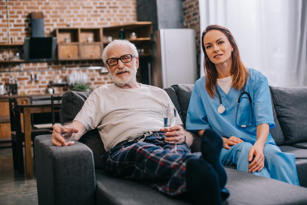 Старший пацієнт з таблетками і медсестрою сидить на дивані
 - Фото, зображення