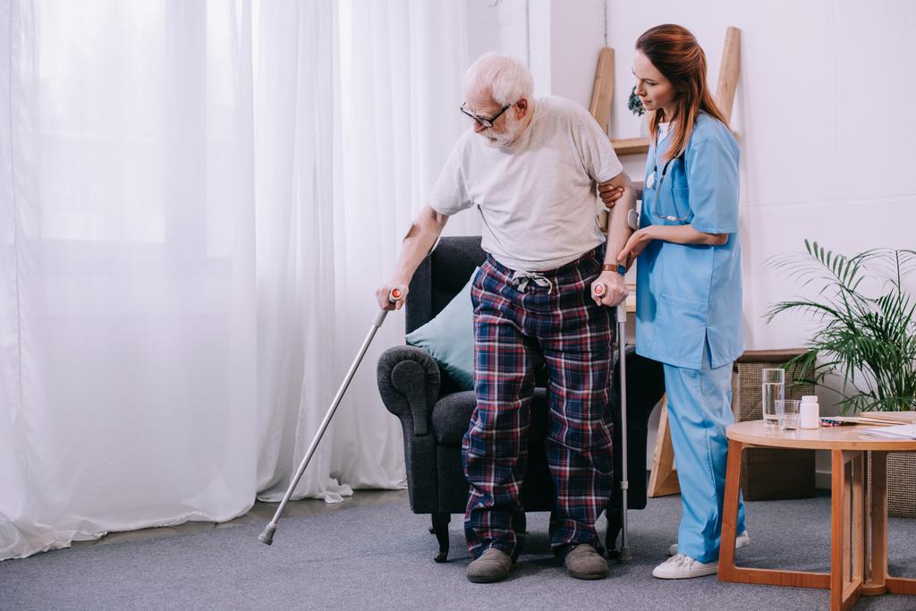 Enfermera ayudando a paciente masculino con muletas
 - Foto, imagen