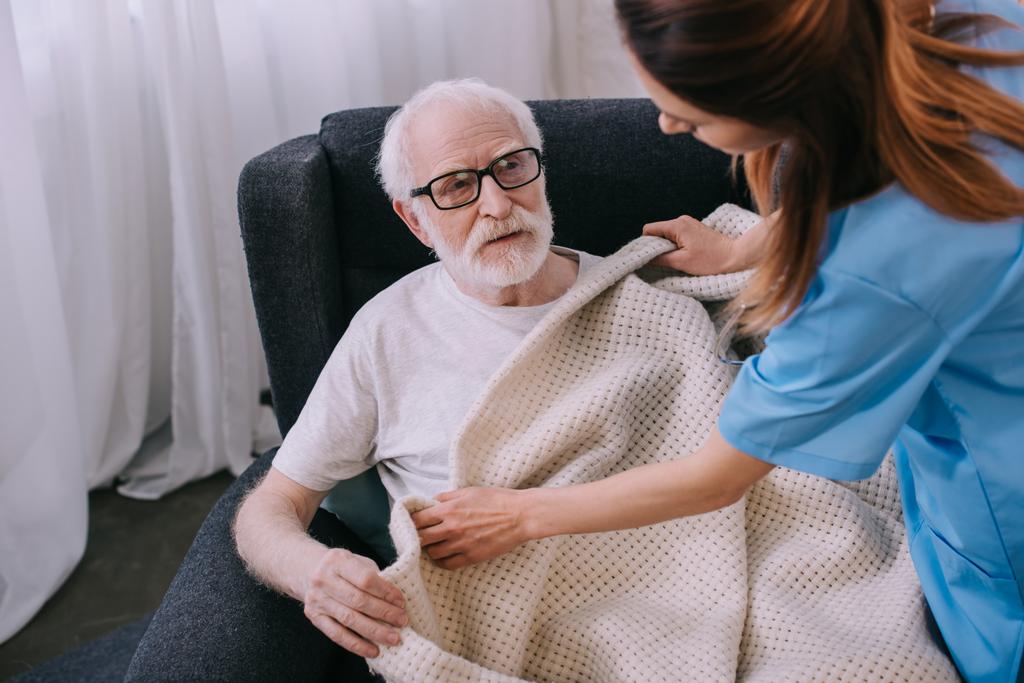 Pflegekraft deckt Seniorin mit Plaid ab - Foto, Bild