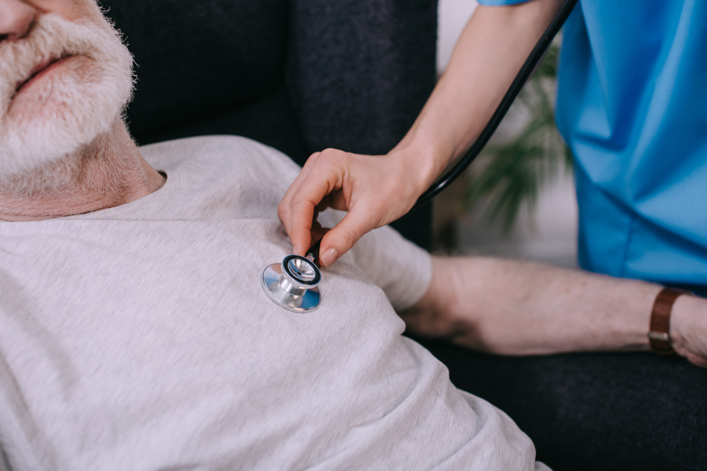 Vue rapprochée d'une infirmière avec stéthoscope vérifiant le rythme cardiaque d'un homme âgé
 - Photo, image