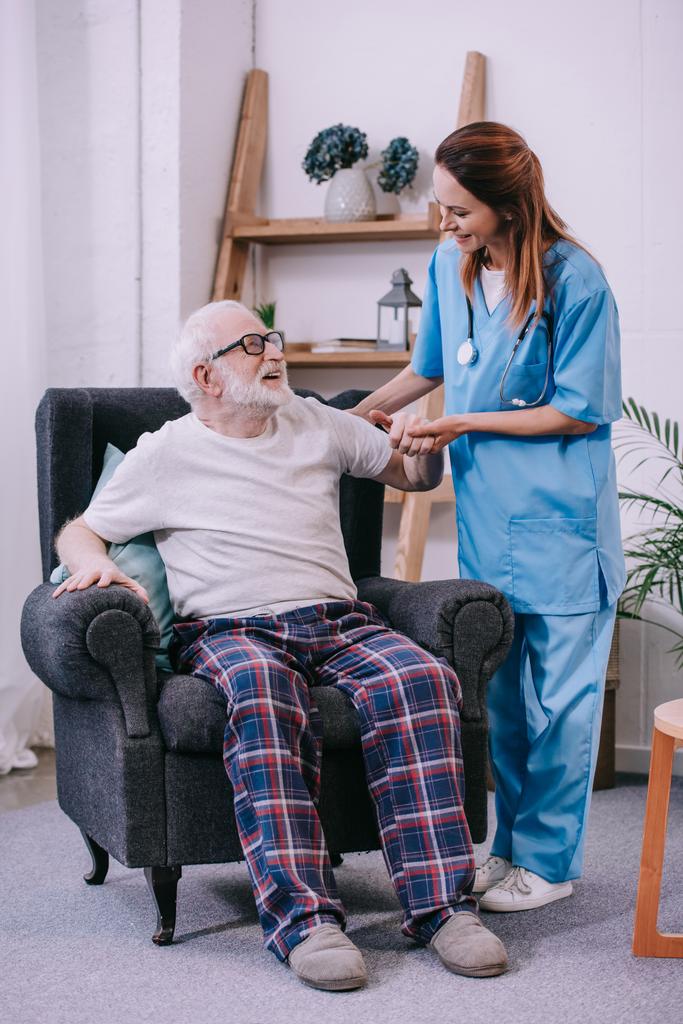 Aide soignant tenant la main d'un patient âgé souriant
 - Photo, image