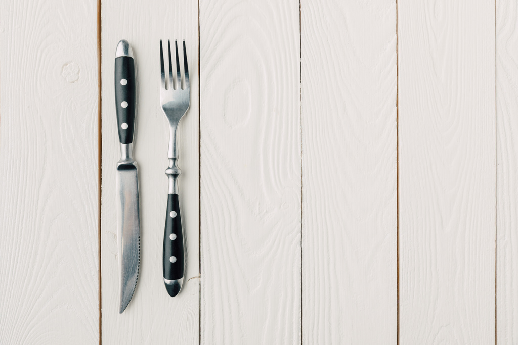 bovenaanzicht van de vork en mes op witte houten achtergrond - Foto, afbeelding