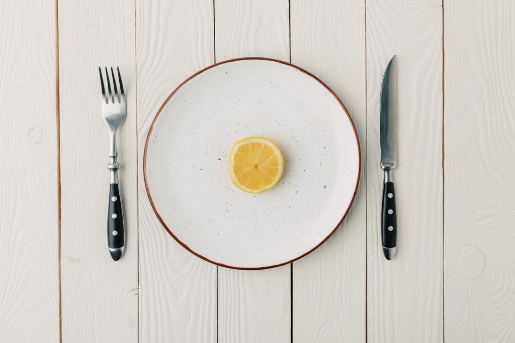 La moitié du citron juteux sur une assiette avec des couverts sur fond de bois blanc
 - Photo, image