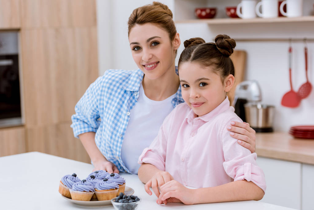 feliz joven madre e hija con cupcakes de arándanos en la cocina
 - Foto, imagen