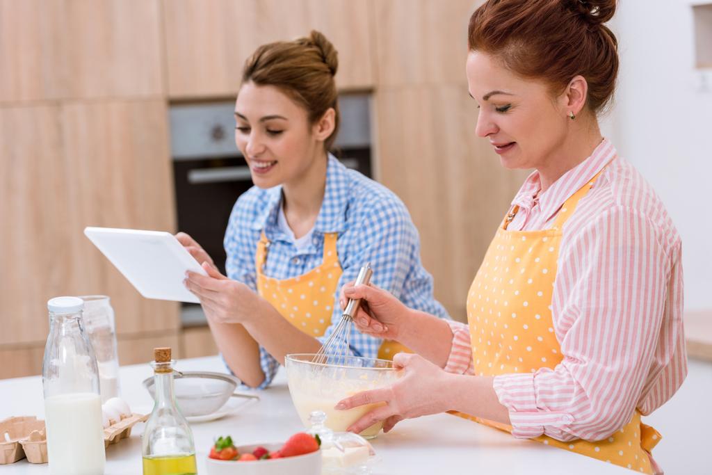 young woman and her mother cooking together at kitchen and using tablet - Photo, Image