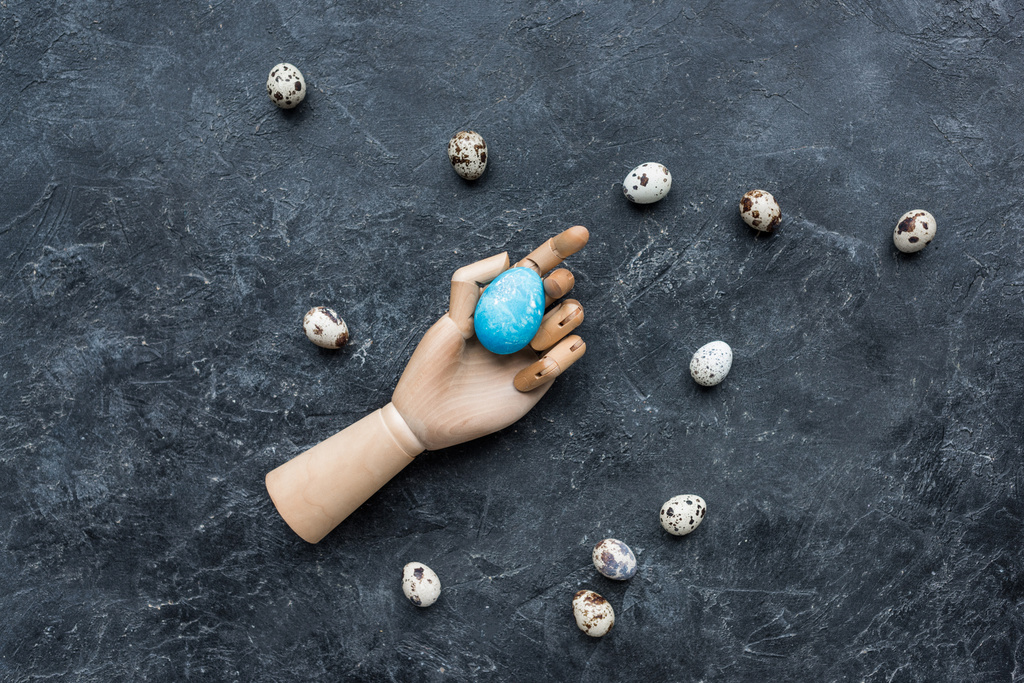Kwarteleitjes rond etalagepop hand met gekleurde ei op donkere achtergrond - Foto, afbeelding