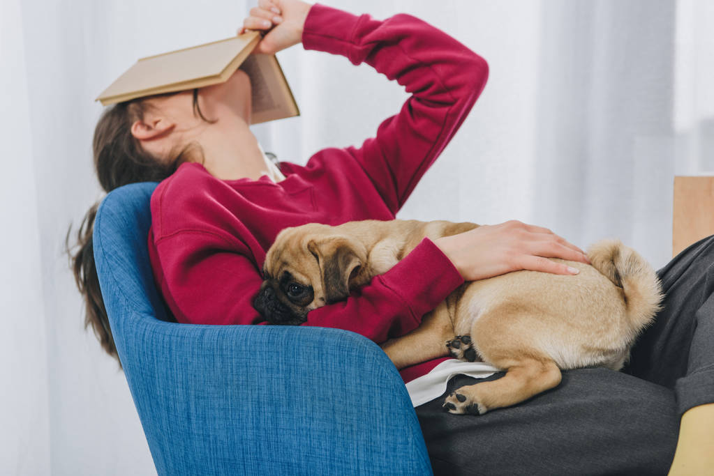 Pretty lady hugging pug and covering her face with book - Photo, Image