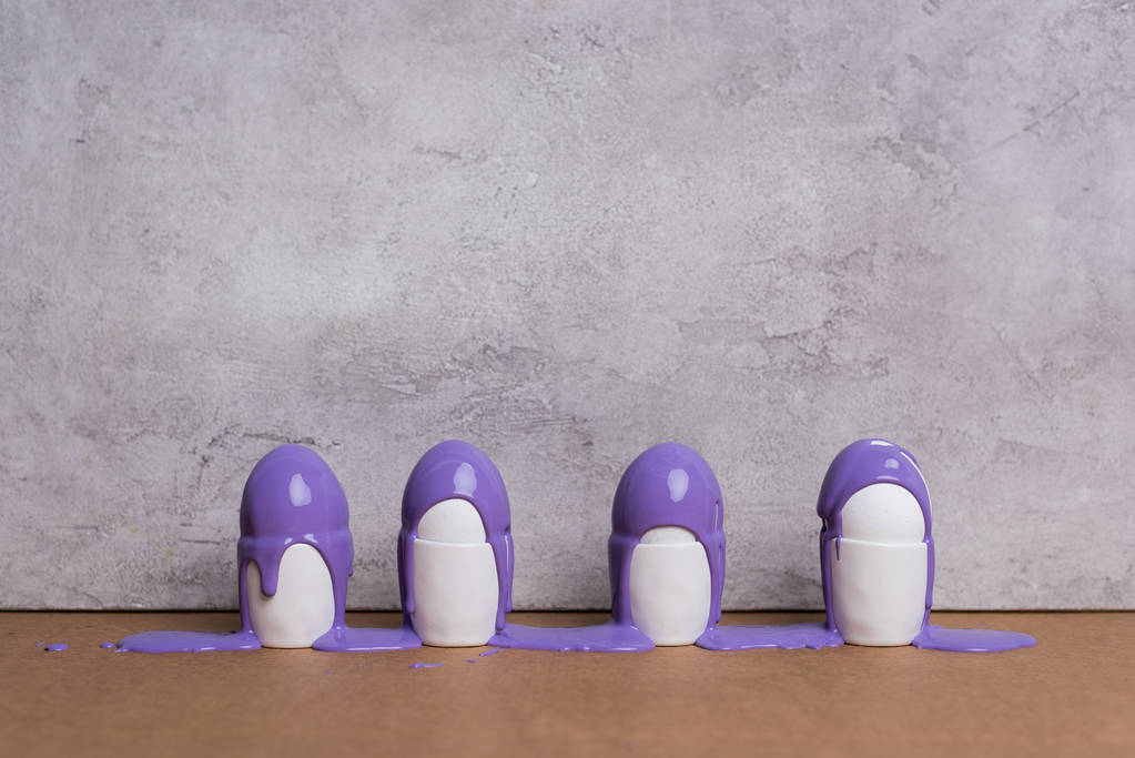 Eieren in kopjes bedekt met paarse verf op grijze achtergrond - Foto, afbeelding