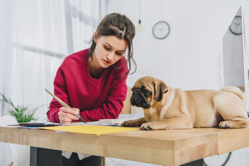 Pretty lady working on illustrations with cute pug on working table with computer - Photo, Image