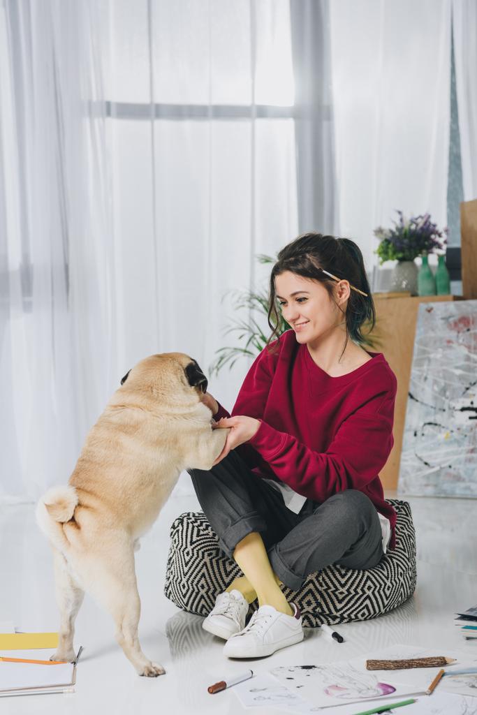 Молодая женщина обнимает симпатичную собаку на полу среди эскизов
 - Фото, изображение