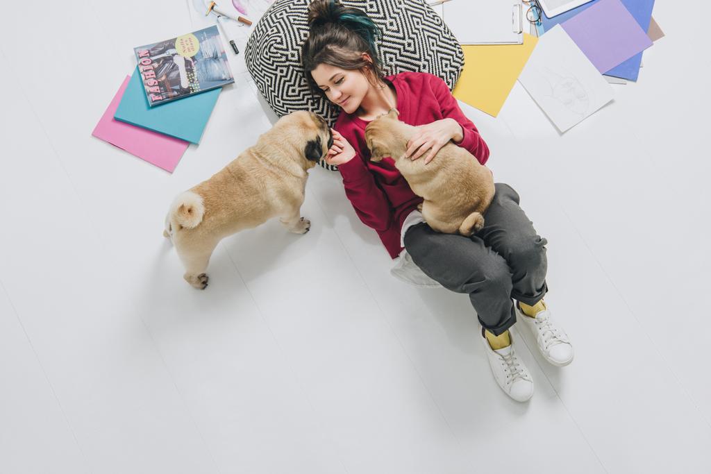 Νεαρή γυναίκα αγκαλιάς pugs στον όροφο, ανάμεσα σε σκίτσα - Φωτογραφία, εικόνα