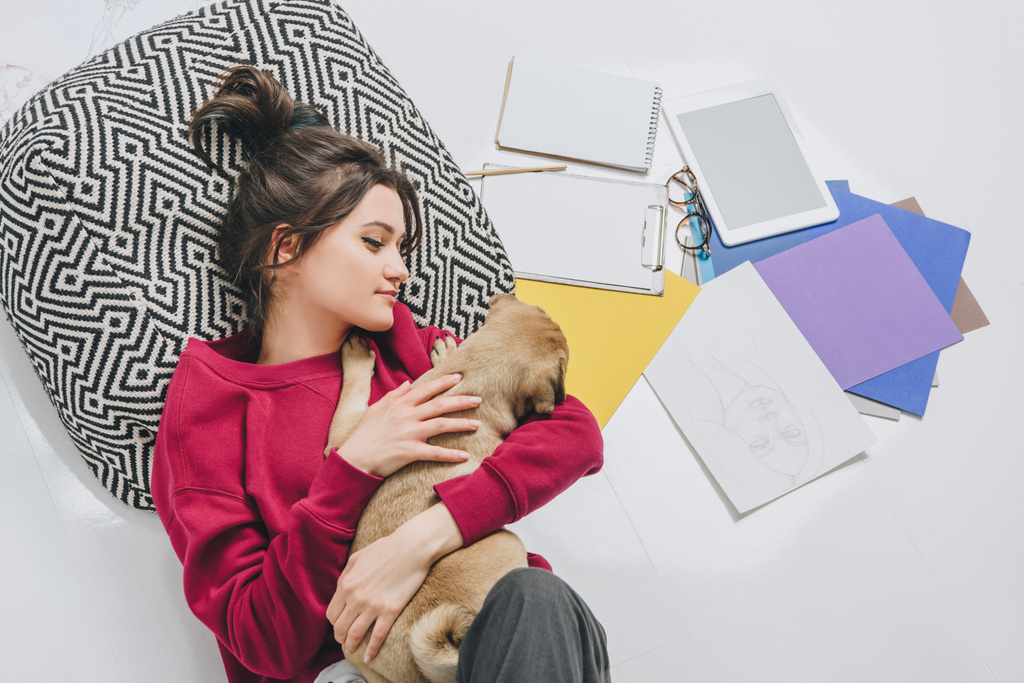 Pretty lady hugging cute dog on floor among sketches - Photo, Image