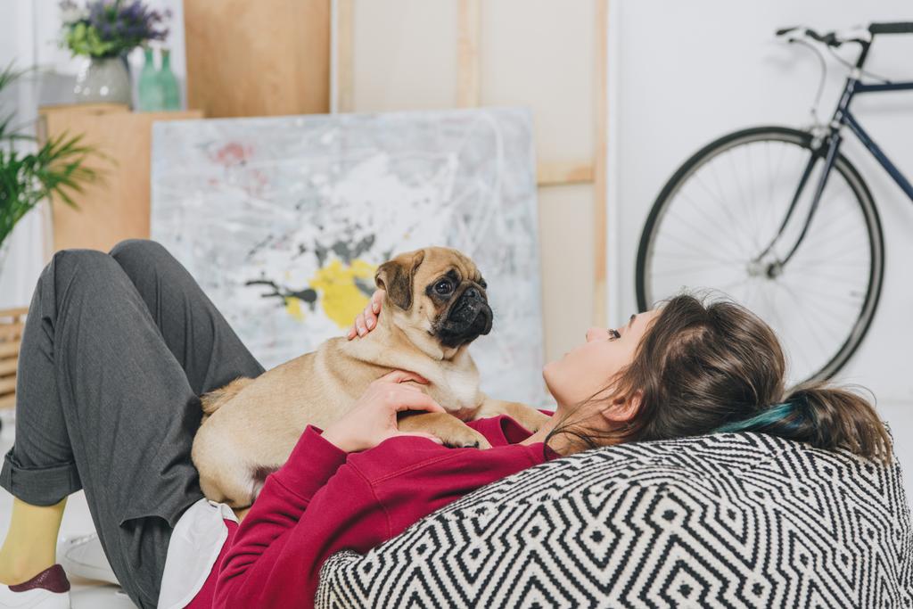Young woman playing with pug puppy on floor of modern room - Photo, Image