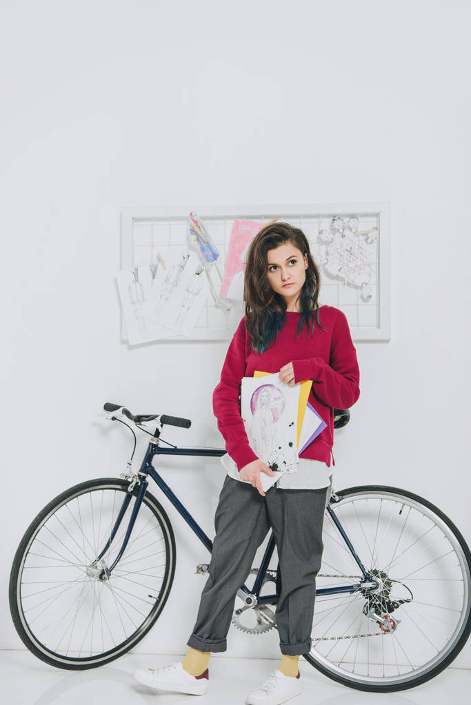 Mujer joven sosteniendo bocetos y de pie en bicicleta
 - Foto, Imagen