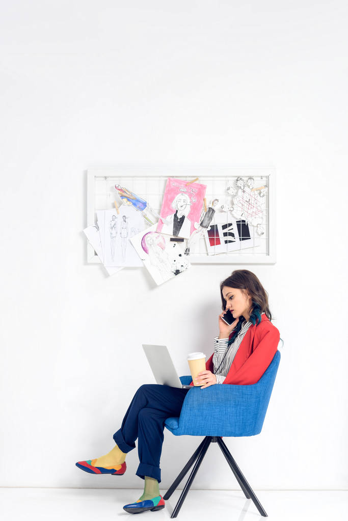 Mujer joven hablando por teléfono mientras trabaja en el ordenador portátil
 - Foto, imagen