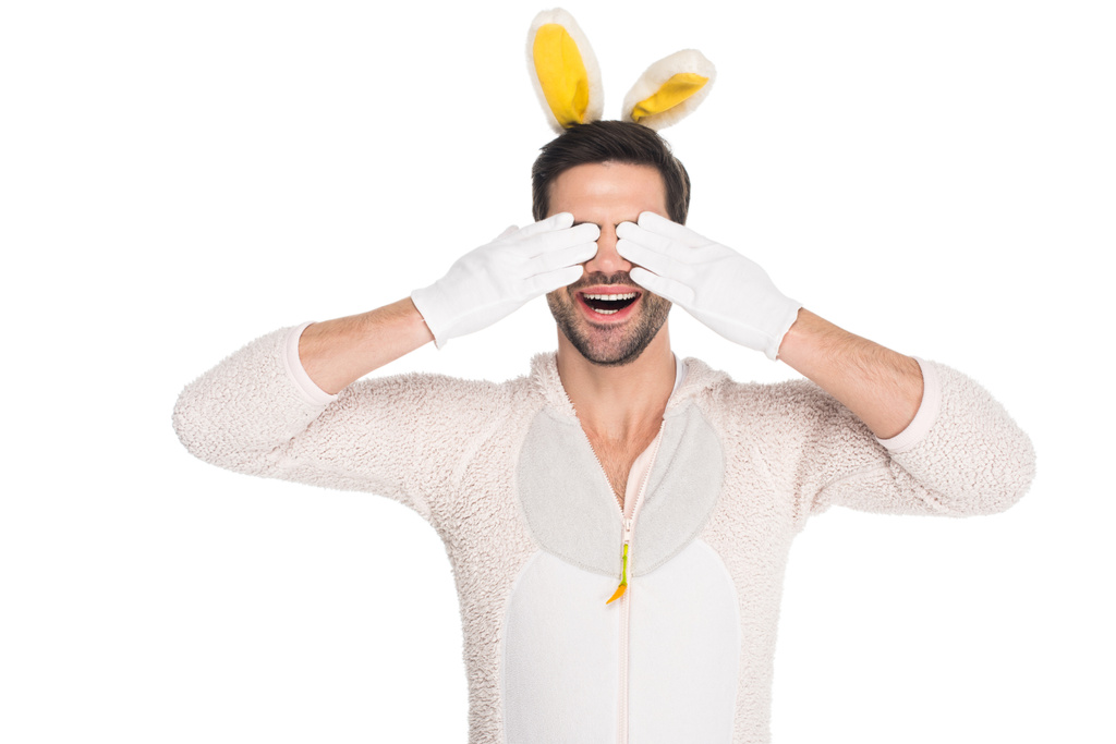 Улыбающийся человек в костюме кролика закрывает глаза руками, изолированными от белого, пасхального понятия
 - Фото, изображение