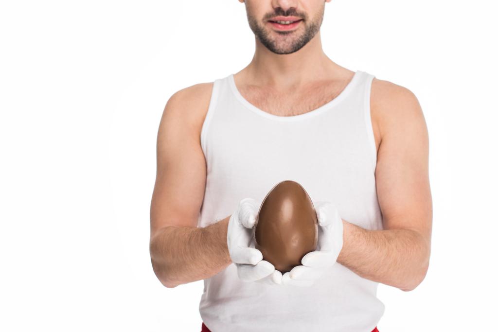 Młody człowiek posiadający duże jajko czekoladowe w ręce na białym tle na biały, koncepcja Wielkanoc - Zdjęcie, obraz