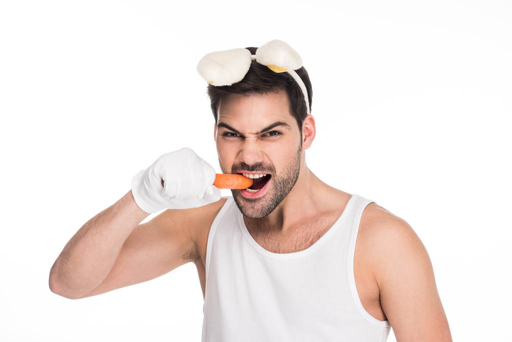 Чоловік з вухами кролика кусає моркву ізольовано на білому, Великодньому концепті
 - Фото, зображення