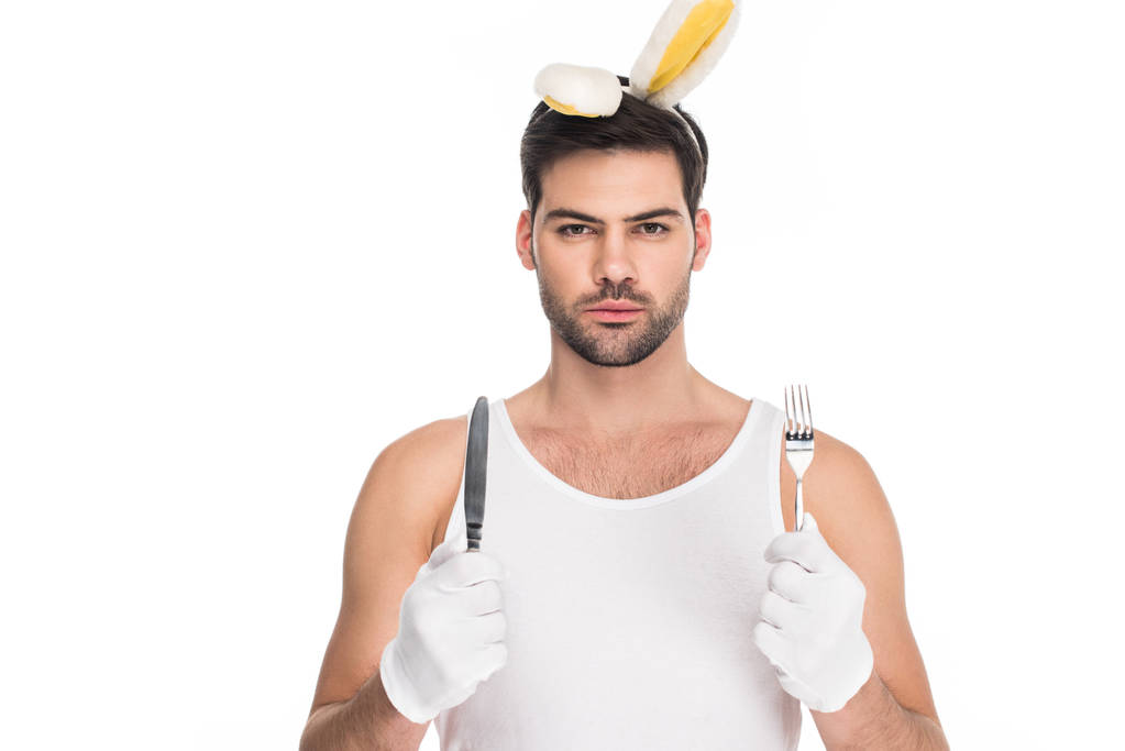 Ritratto di giovane uomo con orecchie da coniglio che tiene la forchetta con coltello isolato su bianco, concetto pasquale
 - Foto, immagini