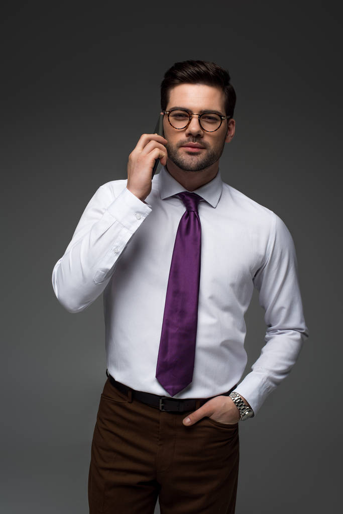 Lächelnder Geschäftsmann mit Brille im Gespräch auf Smartphone isoliert auf grau - Foto, Bild