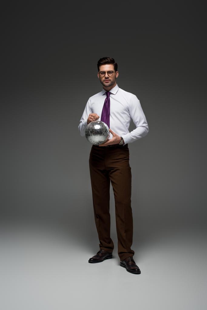 Jonge zakenman in glazen houden glas disco bal op grijs - Foto, afbeelding