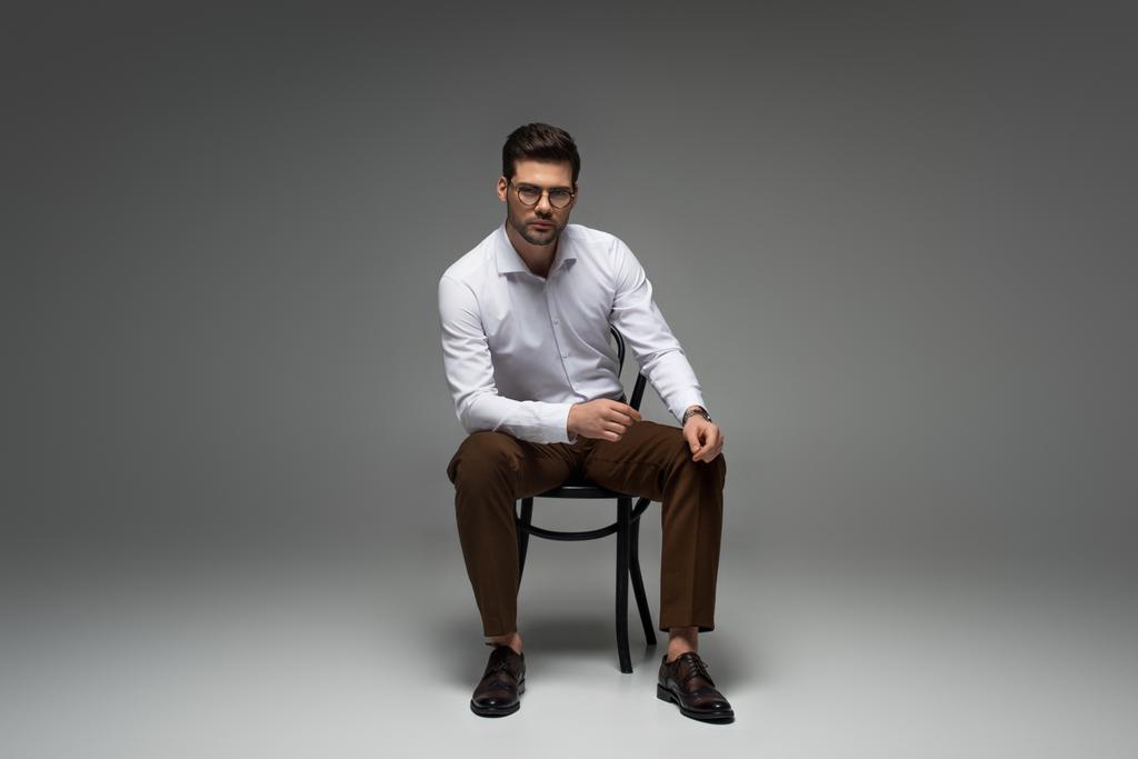 стильний бізнесмен в окулярах сидить на сірому
 - Фото, зображення