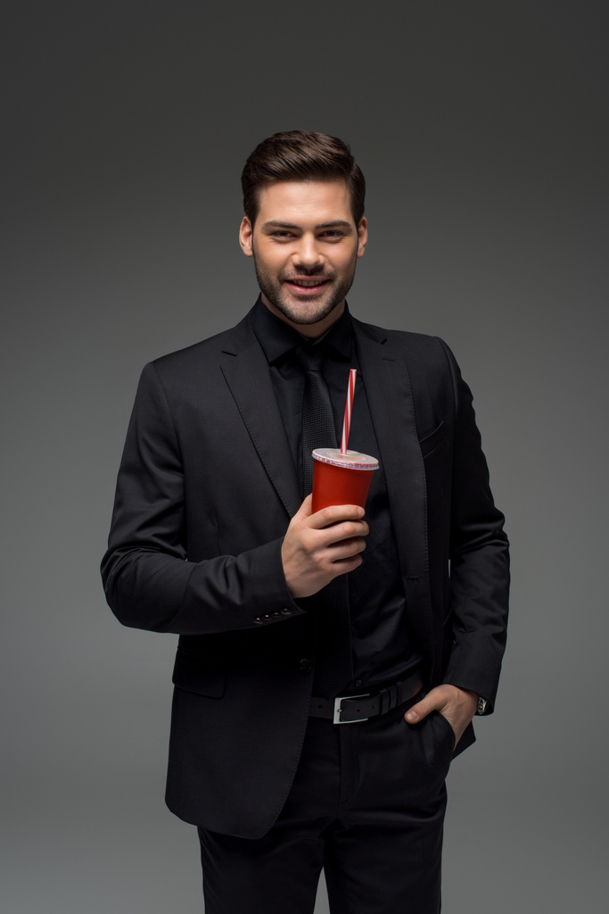 Hombre de negocios sonriente sosteniendo taza desechable aislado en gris
 - Foto, Imagen