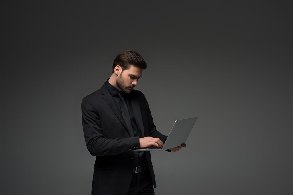 Vue latérale de l'homme d'affaires tapant sur ordinateur portable isolé sur gris
 - Photo, image