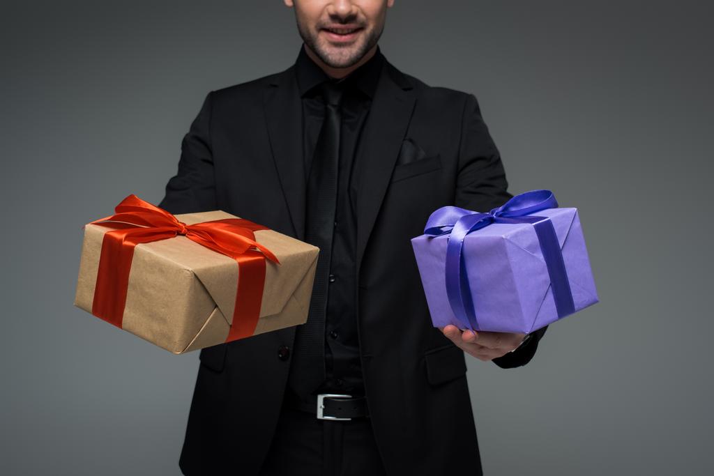 Обрізаний вид чоловіка в чорному костюмі, що тримає дві подарункові коробки ізольовані на сірому, міжнародна концепція жіночого дня
  - Фото, зображення