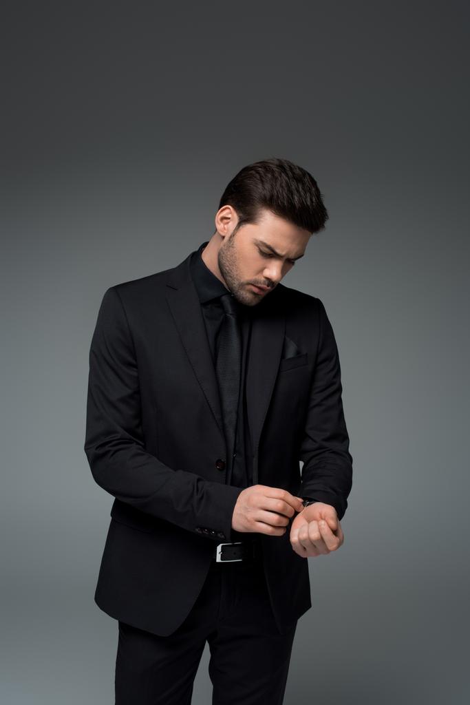 Stylish male in suit correcting wristwatch isolated on grey - Photo, Image