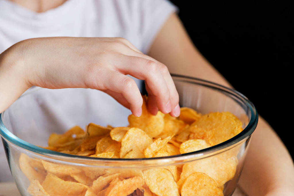 Kinderhand holt Chips aus Glasschüsseln, schädliches Essen - Foto, Bild