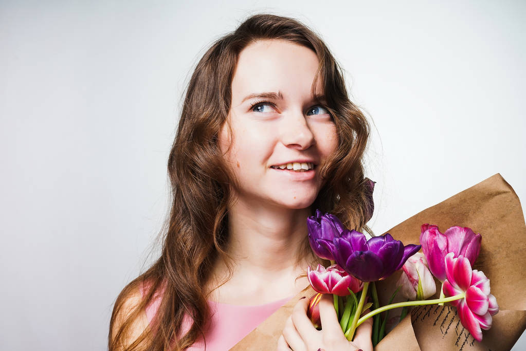 όμορφη νεαρή γυναίκα που κρατώντας ένα μπουκέτο λουλούδια, χαμογελώντας και να σκεφτόμαστε τις διακοπές, μια παγκόσμια ημέρα γυναίκας - Φωτογραφία, εικόνα