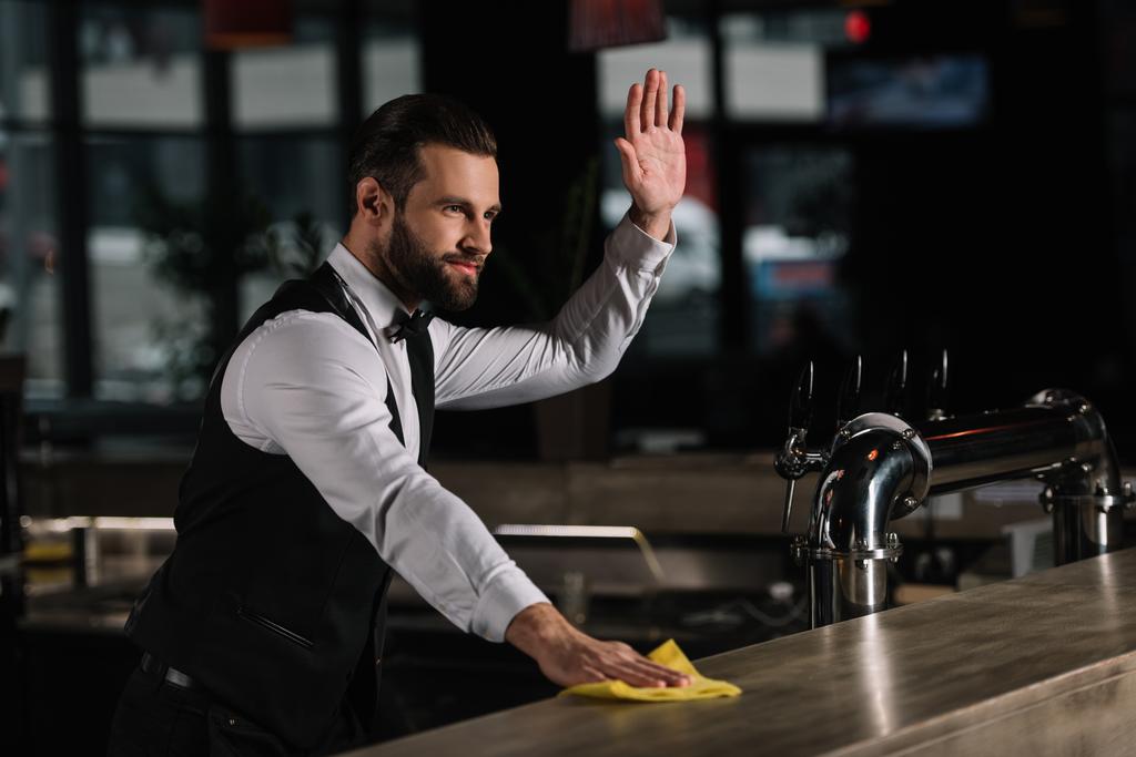 komea baarimikko puhdistaa baari laskuri ja heiluttaa käsi joku
 - Valokuva, kuva