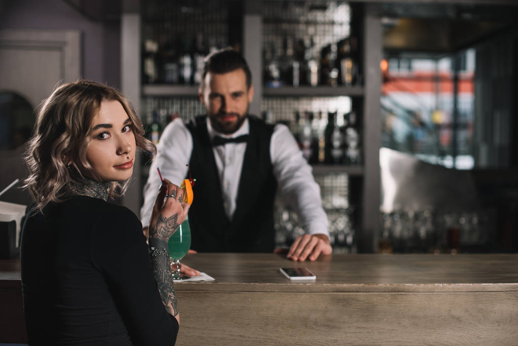 camarero y chica tatuada mirando a la cámara en el mostrador de bar
 - Foto, Imagen