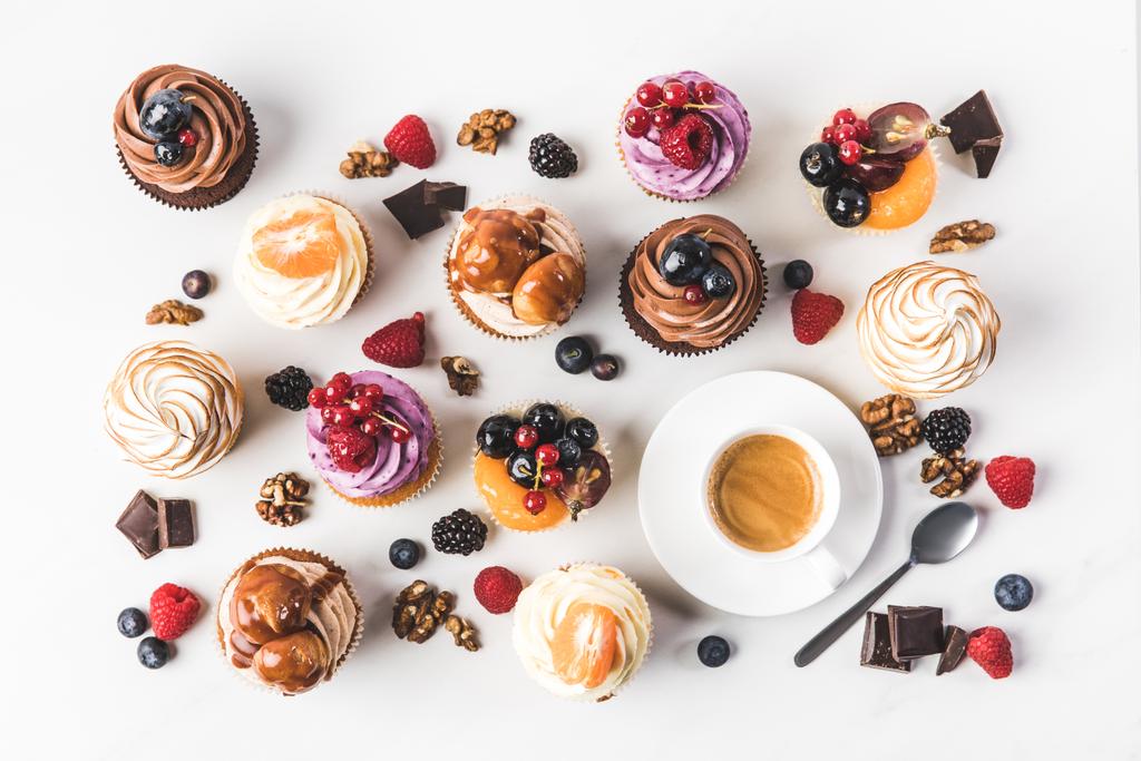 tendido plano con arreglo de cupcakes dulces, cucharadita y taza de café aislado en blanco
 - Foto, Imagen