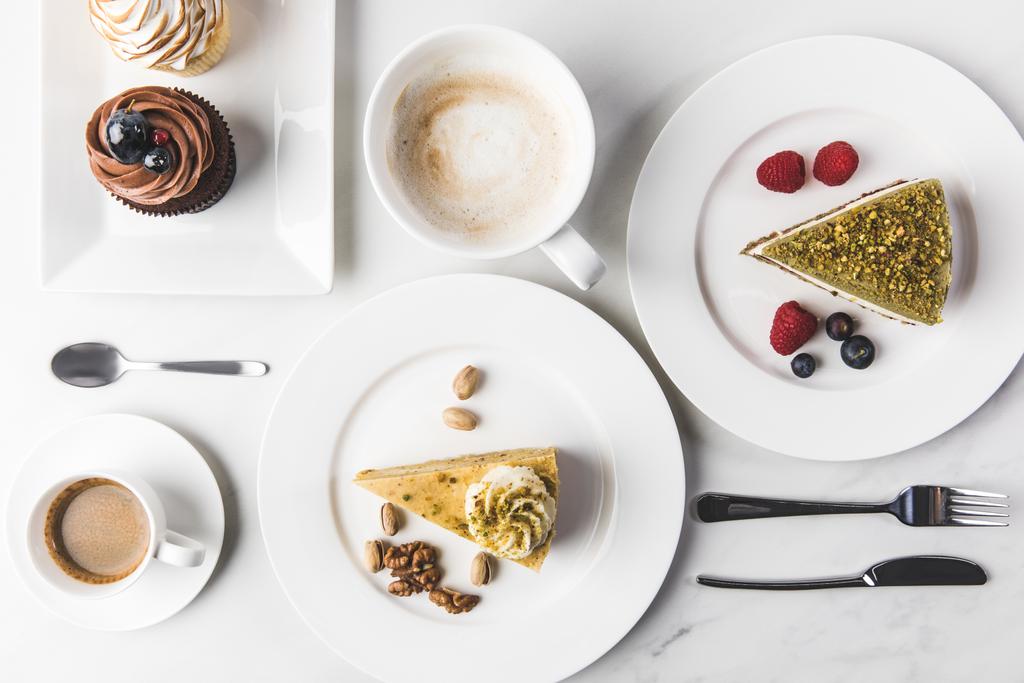Widok z góry układu kawałków różnych ciast na talerze, filiżanki, Kawa i babeczki na białym tle - Zdjęcie, obraz