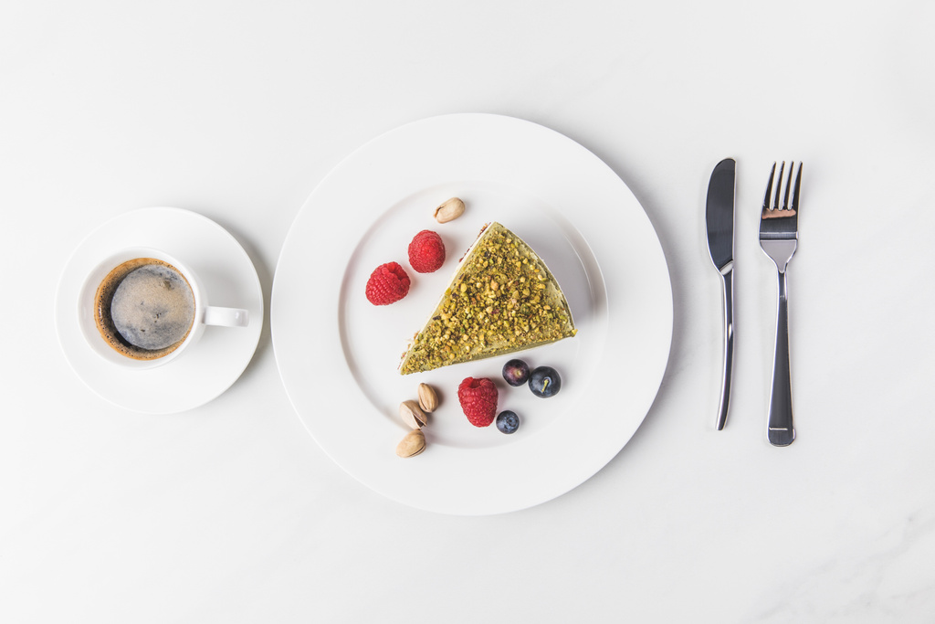 вид сверху на сладкий торт с фисташками и ягодами на тарелке и чашку кофе изолированы на белом
 - Фото, изображение