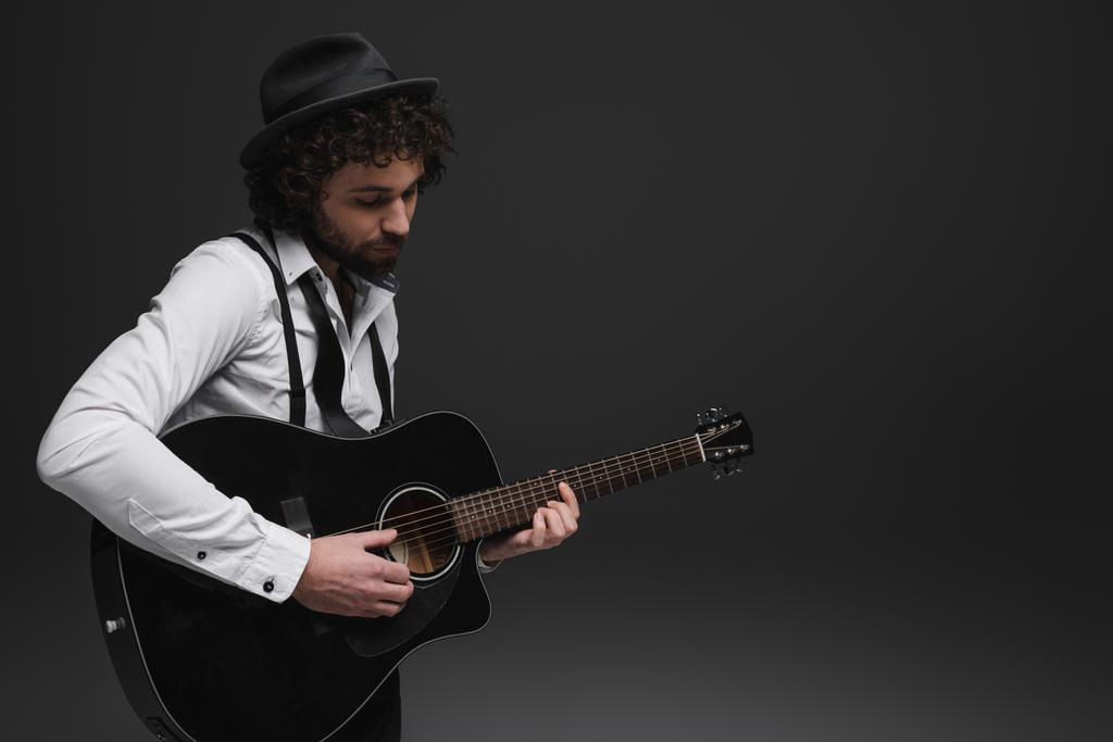handsome bearded musician playing acoustic guitar on black - Photo, Image