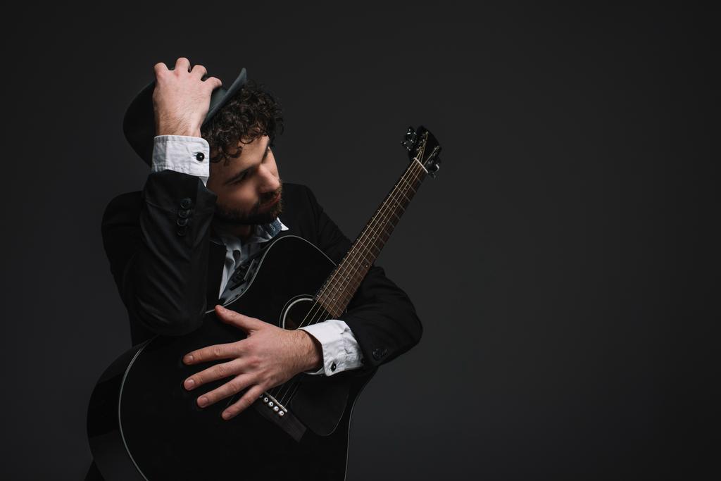 guapo músico en sombrero abrazando su guitarra en negro
 - Foto, Imagen