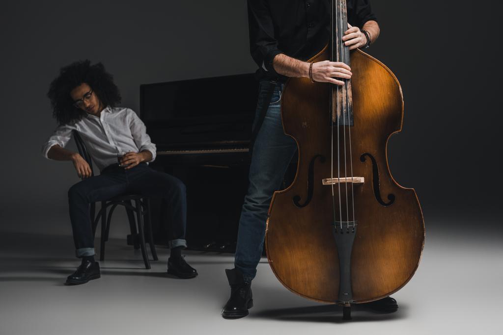 cropped shot of man playing violoncello while his depressed partner sitting at piano blurred on background - Photo, Image