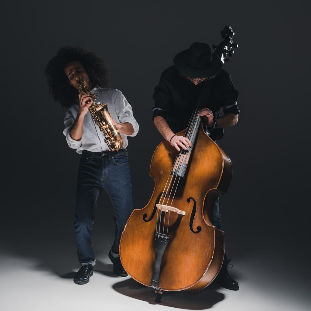 dueto de jovens jazzmen tocando trompete e saxofone no preto
 - Foto, Imagem