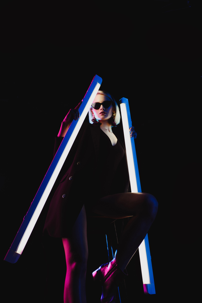 stijlvolle model poseren met twee ultra violet lampen voor mode-shoot, geïsoleerd op zwart - Foto, afbeelding