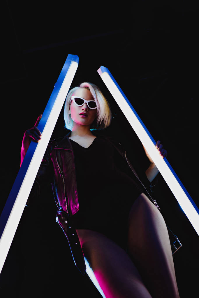 красивая стильная девушка позирует с двумя ультрафиолетовыми лампами, изолированными на черном
 - Фото, изображение