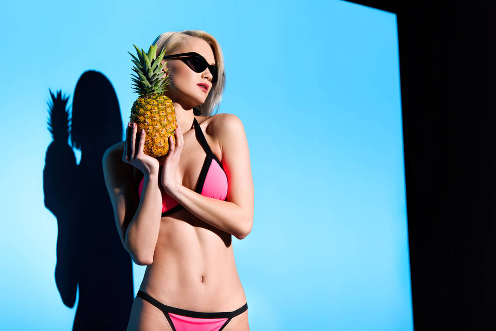 mooi meisje poseren in bikini met ananas voor fashion shoot - Foto, afbeelding