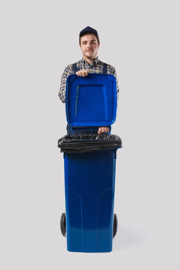 portrait of young cleaner in uniform with trash bin isolated on grey - Photo, Image