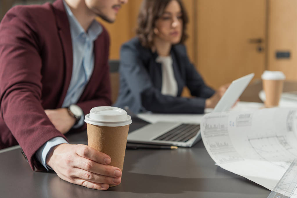 обрезанный снимок бизнесменов с бумажными чашками кофе, работающих с ноутбуком вместе в офисе
 - Фото, изображение