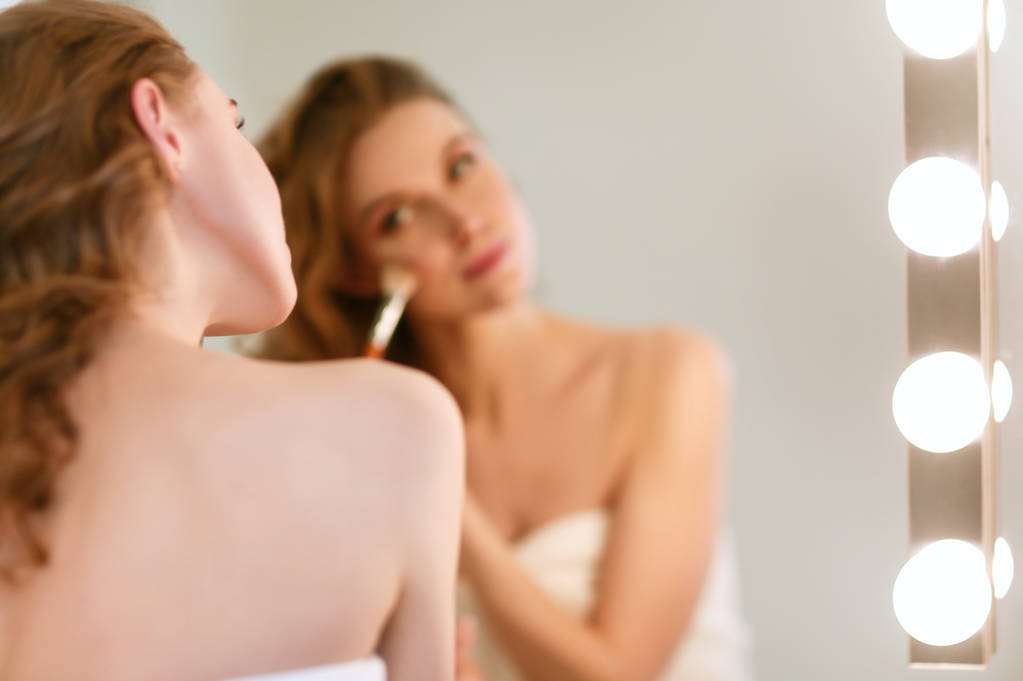 mujer joven mirándose en el espejo y maquillándose. - Foto, imagen